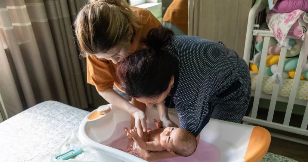 Mother and grandmother bathing newborn baby in a baby bath