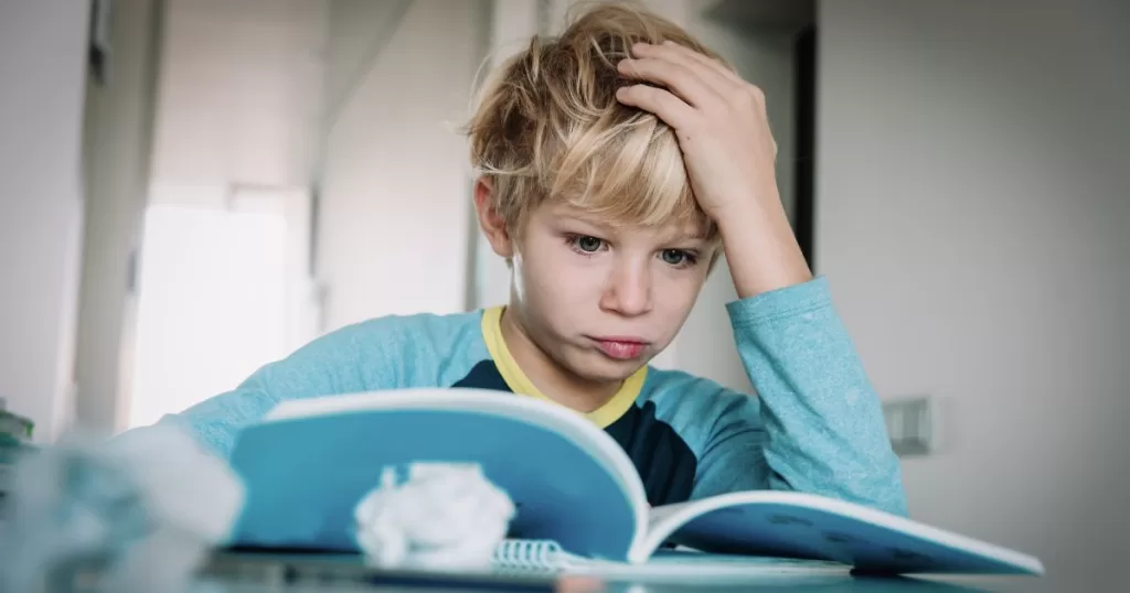 A young boy with a serious expression, holding his head while reading a book, appearing to struggle with understanding the content.