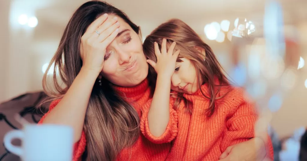 A mother and child, both dressed in matching orange sweaters, look overwhelmed and frustrated, each with their hand on their forehead, conveying a sense of shared stress or confusion.